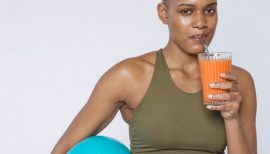 femme de couleur tenant un ballon fitness sous le bras et buvant un jus de fruit