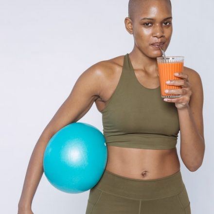 femme de couleur tenant un ballon fitness sous le bras et buvant un jus de fruit