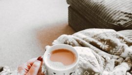 femme en hiver tenant un mug sur ses genoux couverts d'un plaid