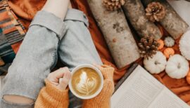 Pumpkin spice latte posé sur les jambes d'une femme entourée de citrouilles et d'un livre