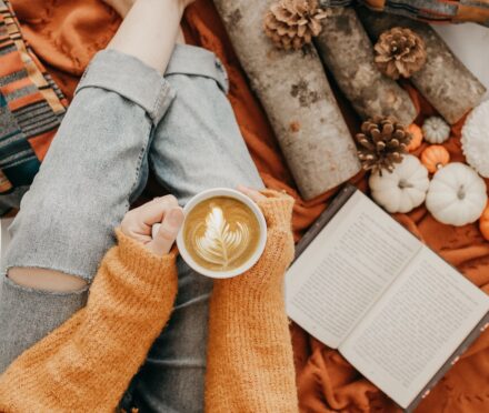 Pumpkin spice latte posé sur les jambes d'une femme entourée de citrouilles et d'un livre