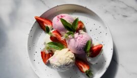 assiette sur laquelle sont posées 3 boules de glace et des morceaux de fraises ainsi que des feuilles en déco
